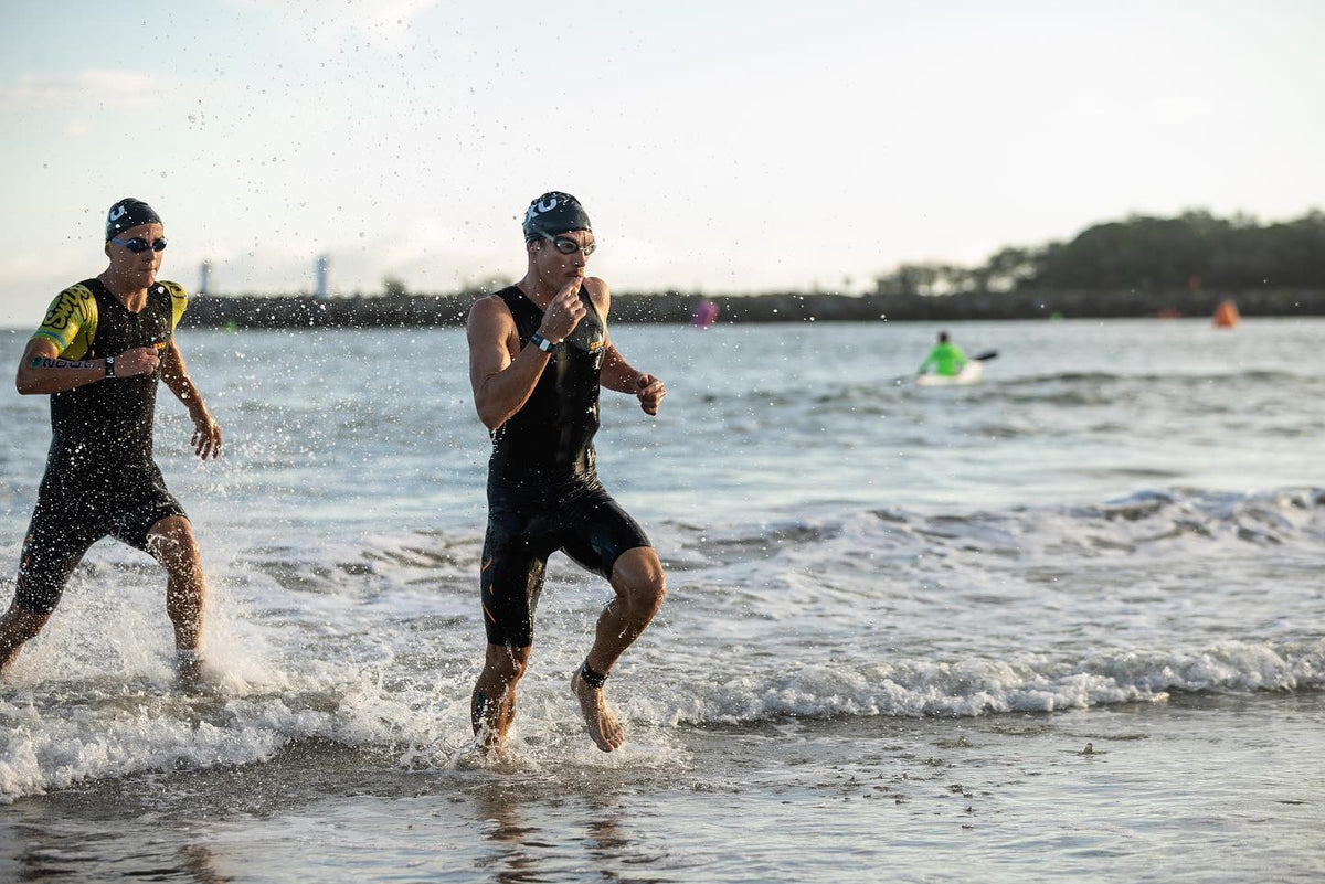 Triathletes running out of the water in wetsuits at the swim exit